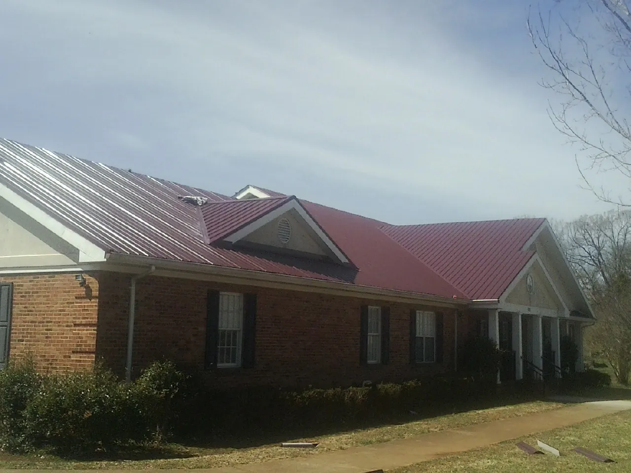 Red metal roof with gabled entries on a long brick building, from a Hail Damage Roof Repair job in Mercer