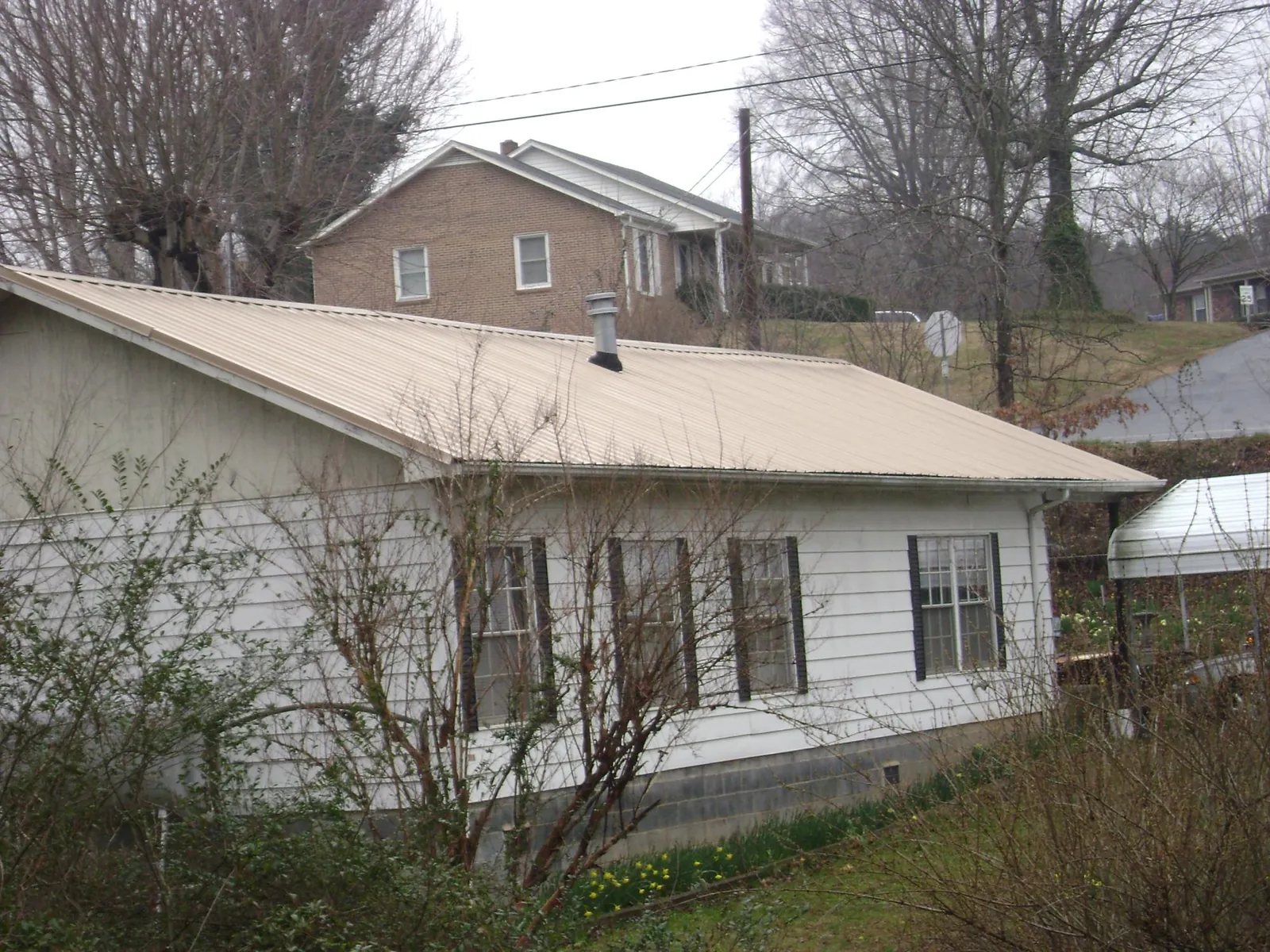 Tan metal roof on a white sided house set into a hillside — Commercial Roofing by Roofing Brothers in Mercer